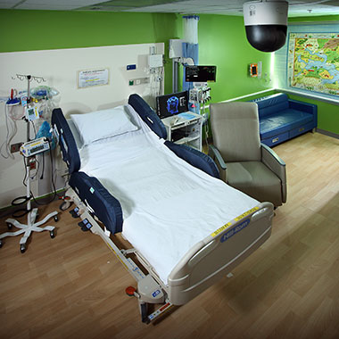 A bed in the new pediatric epilepsy monitoring unit with a computer, medical devices and IV pole next to it, a lounge chair and couch are next to bed and a world map hangs on the wall in the background.