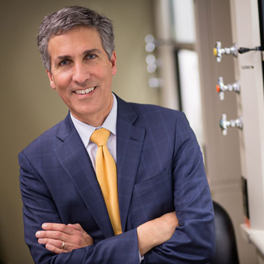 Neurologist and ALS Clinic co-director Nicholas Maragakis, pictured in a lab setting wearing a blue plaid suit, crossing his arms and smiling.