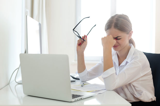 A young woman closes her eyes in pain during break from looking at the computer
