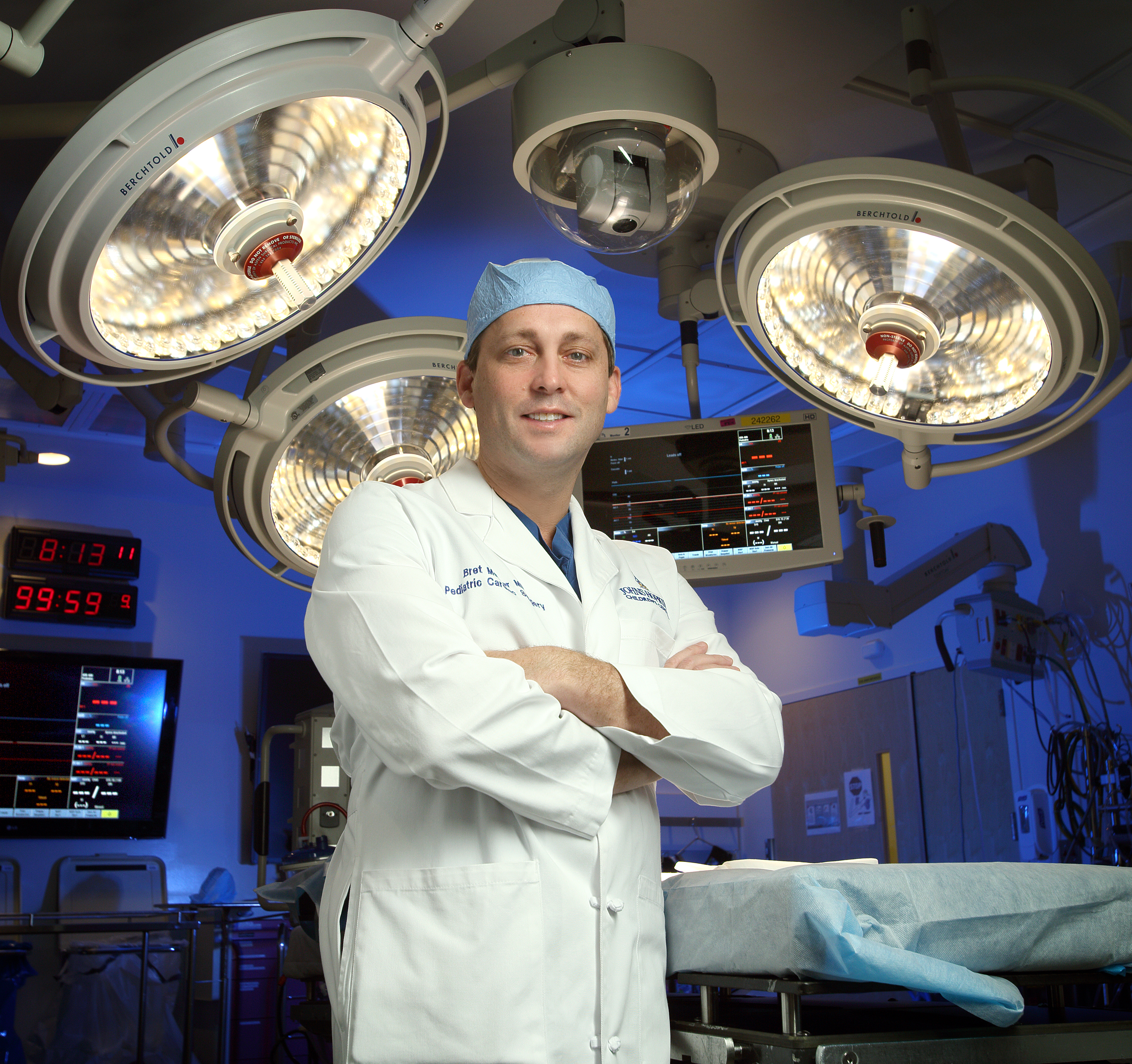 Bret Mettler is in operating room with arms crossed, standing in front of lighting and medical equipment. 