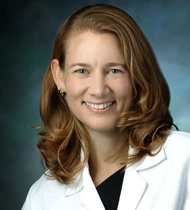 Dr. Brandi Page, smiling in a formal portrait, wearing a white lab coat with a black blouse underneath.