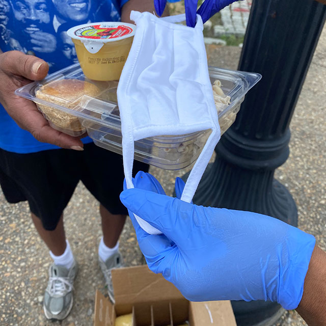 hands on a lunch box, with a sandwich, apple sauce and a mask