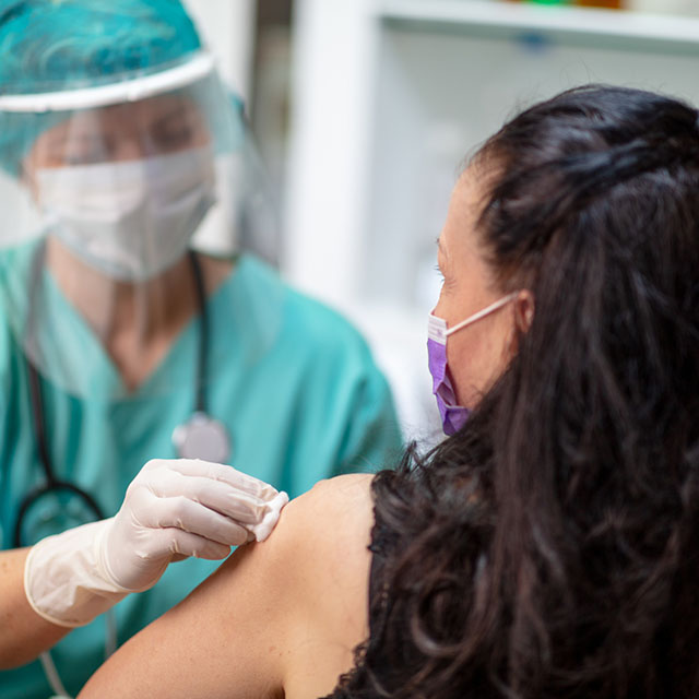 clinician with mask and face shield giving shot to a woman in a mask