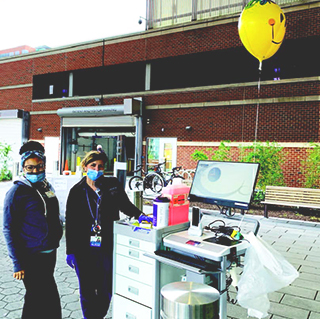 Two nurses standing outside with masks and testing mobile station. 