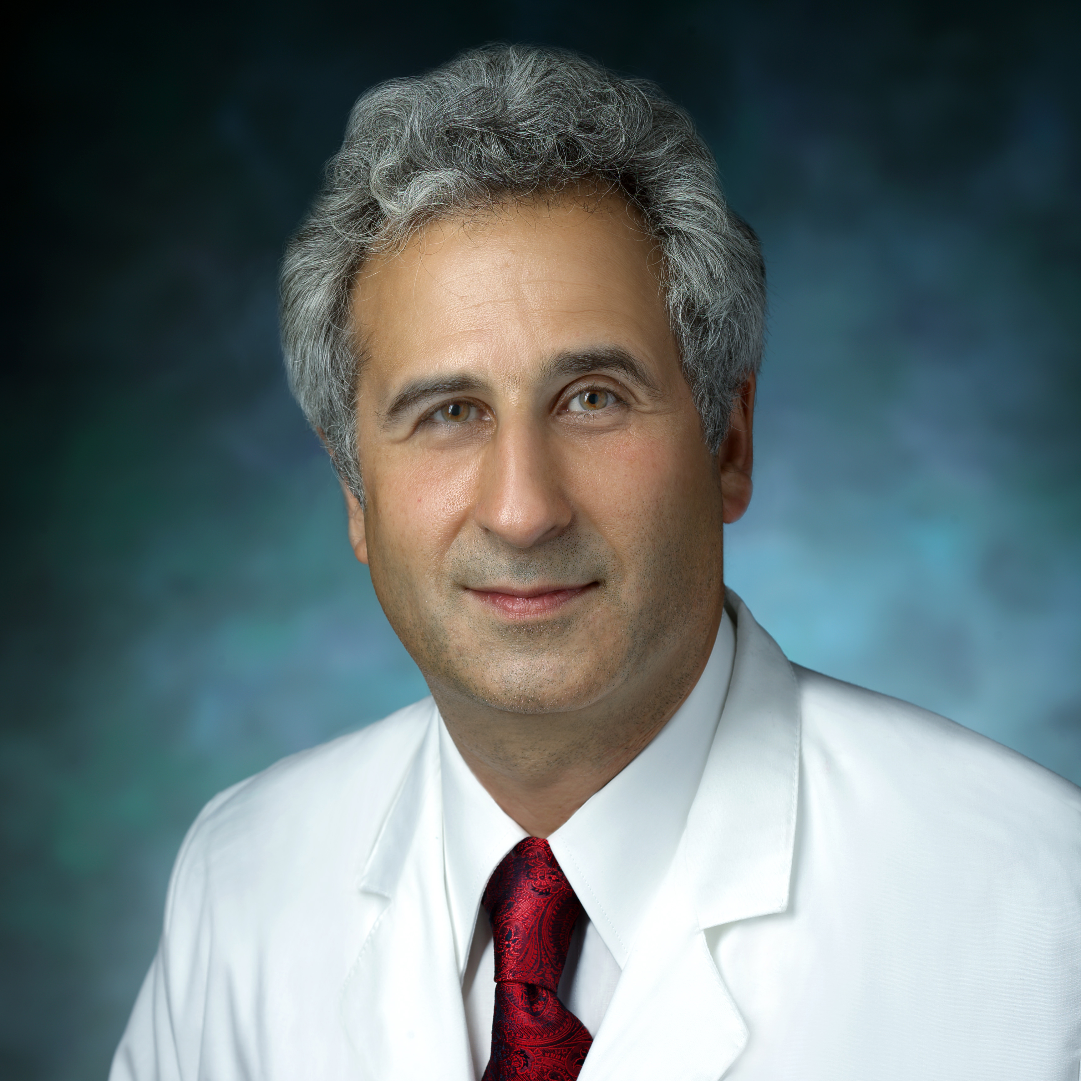 Ahmet Baschat, in a formal portrait, wearing a white lab coat, white button down shirt and red tie.