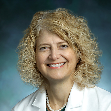 Pediatric neurosurgeon Dody Robinson, in a formal portrait, wearing a white lab coat, green shirt and pearl necklace.
