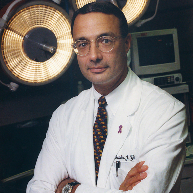 Charles Yeo standing with arms crossed in front of large circular lights in an operating room.