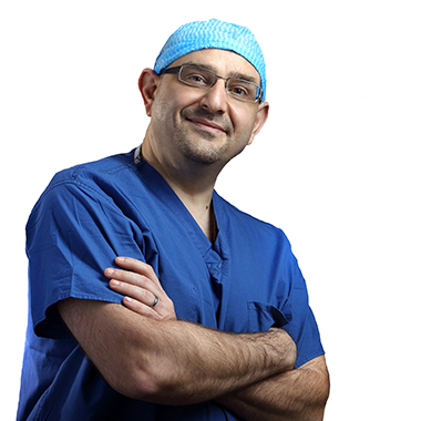 Bashar Safar, chief of colorectal surgery, wearing blue scrubs and a surgical cap on a white background.