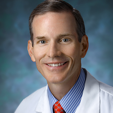 Thoracic surgeon Richard Battafarano in a formal portrait wearing a white lab coat, blue and white striped button down shirt and red tie.