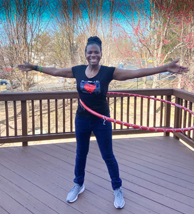 Monica House on her deck, hula hooping with trees in the background showing signs of spring buds