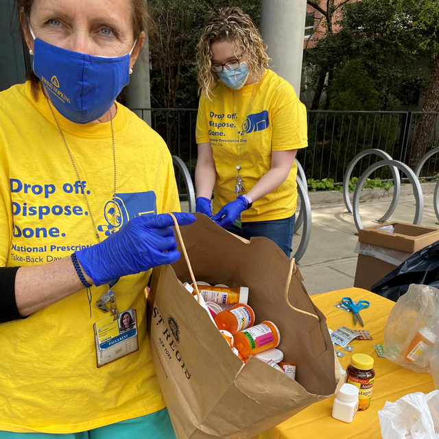 Photo: Patient safety specialist Paula Kent (left) prepares to dispose of a bag of unwanted prescription medications dropped off at the Johns Hopkins Outpatient Center on Prescription Drug Take-Back Day. Pharmacy division director and event organizer Meghan Swarthout punches pills out of their blister packets and into a barrel destined for incineration. 