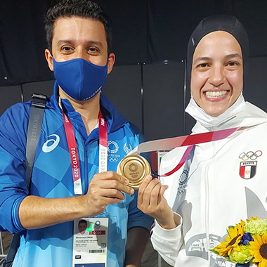 Photo of Emam wearing a mask, standing with an Egyptian athlete. The two hold a bronze medal.