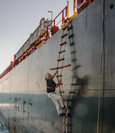 Jorge Viso climbs a rope ladder to board a large container ship. 