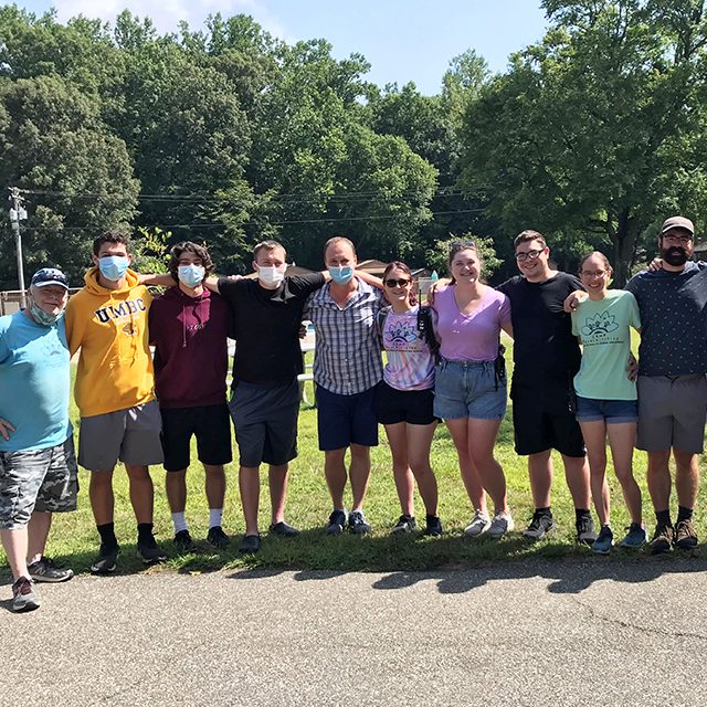 Endocrinologist Mihail Zilbermint, wearing a blue plaid shirt, blue shorts and a surgical mask, poses for a group photo with counselors and recreational staff at Camp Possibilities.