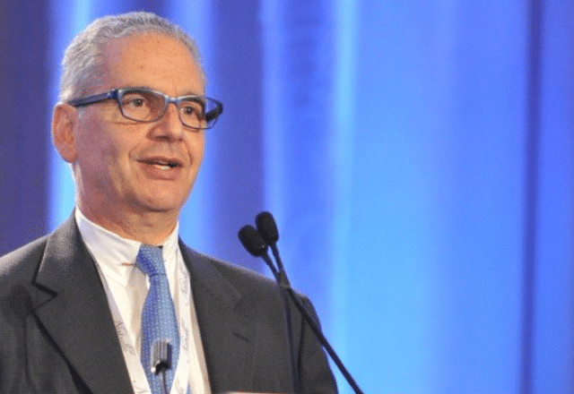 Nagi Khouri standing in front of a podium in a suit. 
