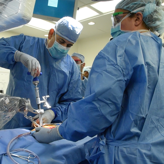 Nicholas Theodore, in an operating room wearing a surgical gown, camp and gloves, performs a robotic spine surgery