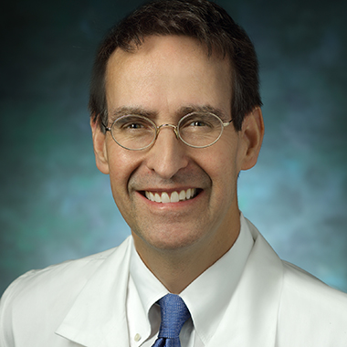James Gammie, in a formal portrait, wearing a white lab coat, white button down shirt, light blue tie and oval glasses