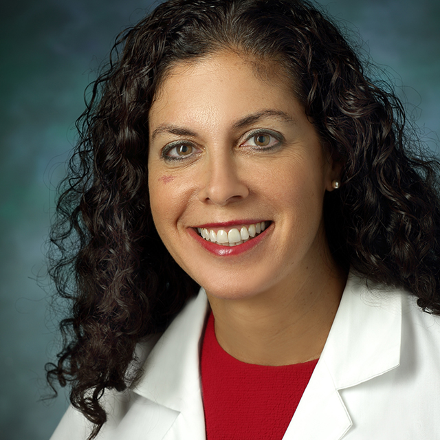 Lilah Morris-Wiseman in a formal portrait wearing a white lab coat, red blouse and pearl earrings