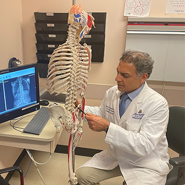 Khaled Kebaish, in a white lab coat, pointing at a model spine.