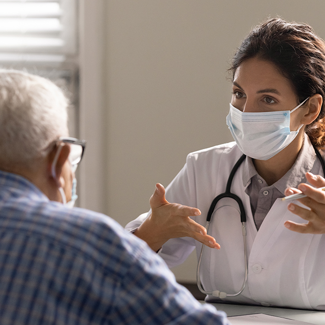 Close up of female doctor wearing face mask, discussing medical results with older man