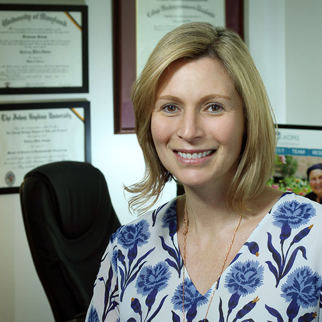 Quincy Samus, in her office, wearing a white blouse with blue flowers on it