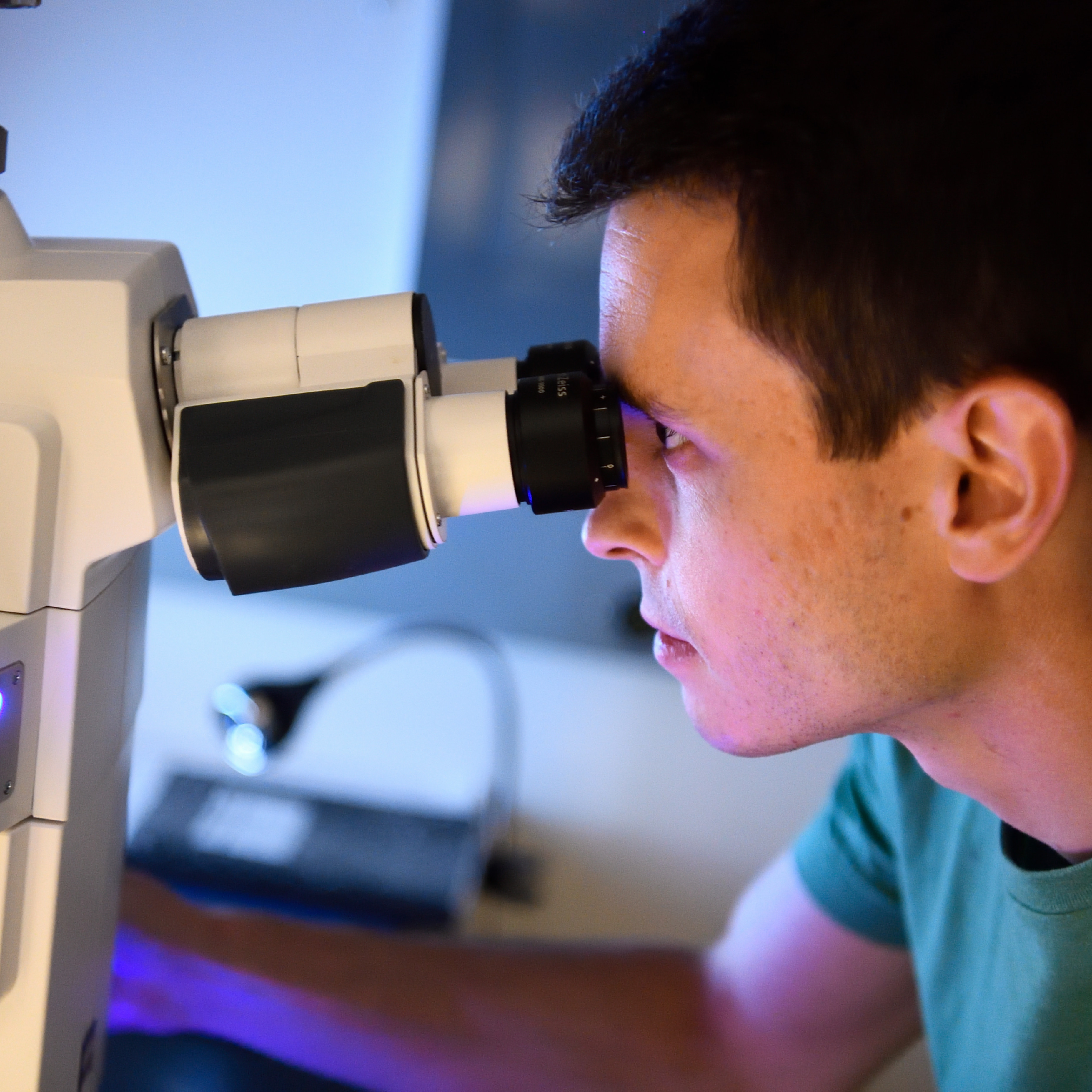 White male student looking into beige microscope