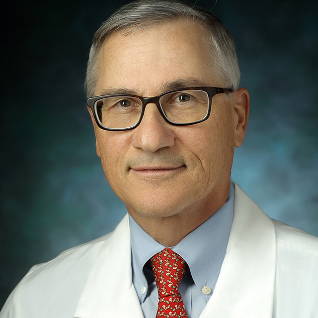 Gerald Andriole, in a formal portrait, wearing a white lab coat, light blue button shirt and red tie