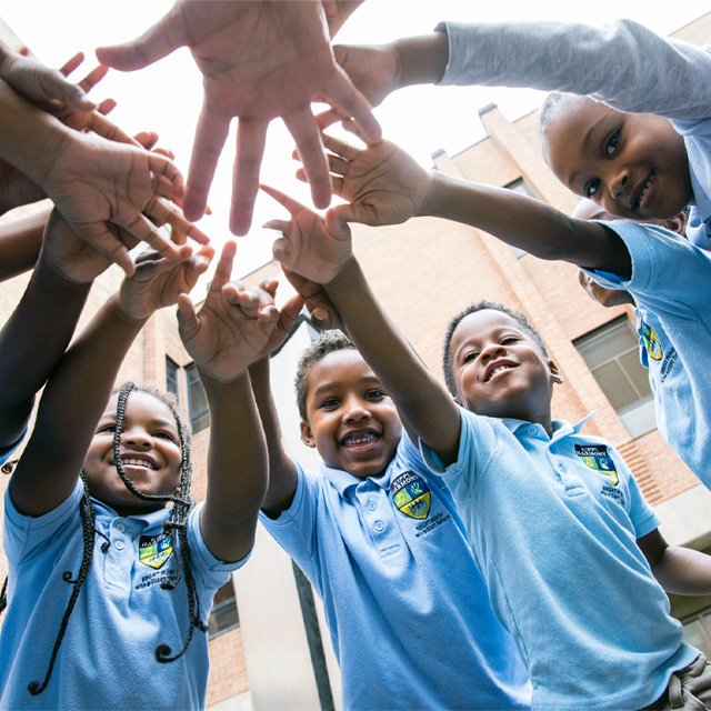 Smiling KIPP students stand in a circle. They all reach their hands into the center of the circle.