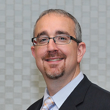 Scott Newsome wearing a black suit and striped tie.
