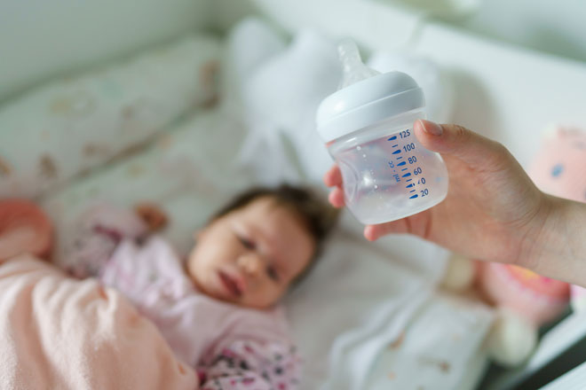 A caretaker holds in empty baby bottle while baby sleeps