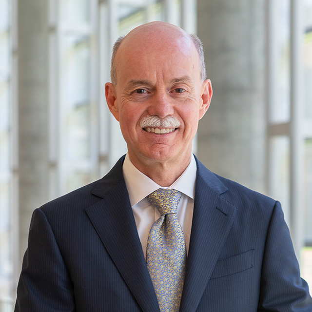 image of Ted DeWeese smiling, in a blue suit with a tie