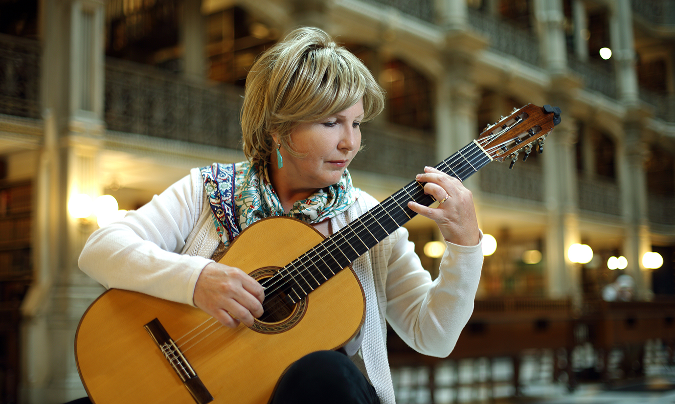 Serap Bastepe-Gray playing a classical guitar inside the George Peabody Library