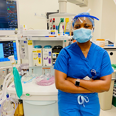 Juliet Gabriel poses in the operating room wearing blue scrubs, a surgical mask and cap