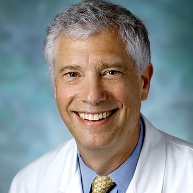 Allan Belzberg, in a formal portrait, wearing a white lab coat, light blue button down shirt and yellow tie