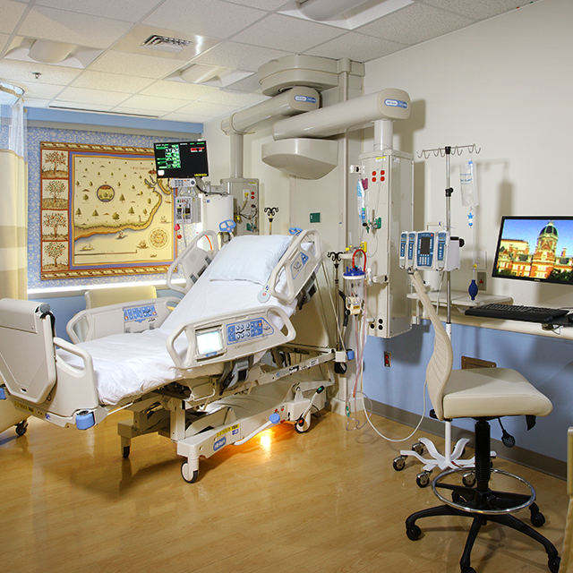 A patient room in the NCCU with a bed, various medical equipment and a desk with a computer and chair