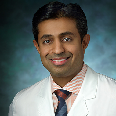Savyasachi Thakkar in a formal portrait, wearing a white lab coat, orange and white striped button down shirt and orange and blue tie
