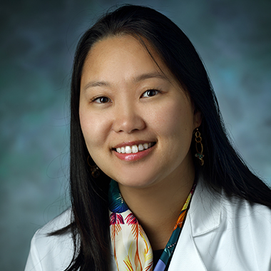 Joon-Yi Kang, in a formal portrait, wearing a white lab coat and multi-colored scarf
