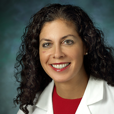Lilah Morris-Wiseman in a formal portrait wearing a white lab coat, red blouse and pearl earrings