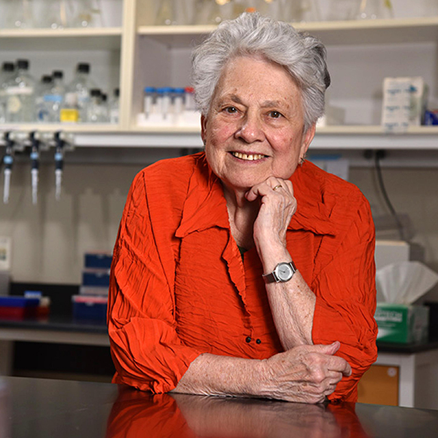 Barbara Migeon leans against a lab counter wearing a red blouse.