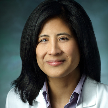 Gina Adrales, in a formal portrait, wearing a white lab coat and light purple button down shirt