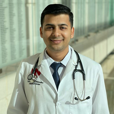 Sagar Chapagain, smiling, wearing a white coat, with a stethoscope around his neck. 
