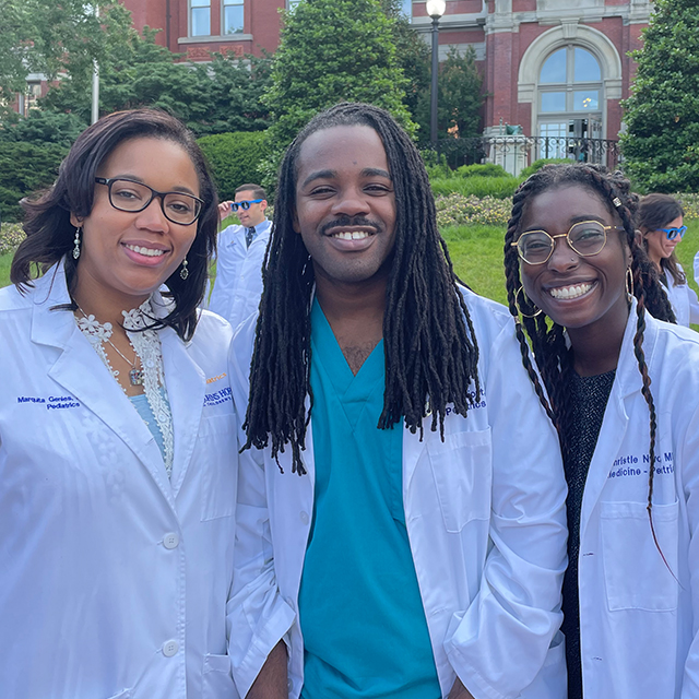 Three students in white coats stand in front of the Billings Building
