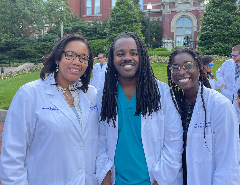 Three students in white coats stand in front of the Billings Building
