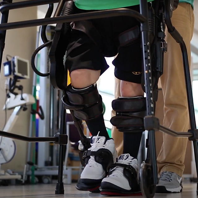 A person with a knee brace is being assisted with the help of a specialist and a walker. 
