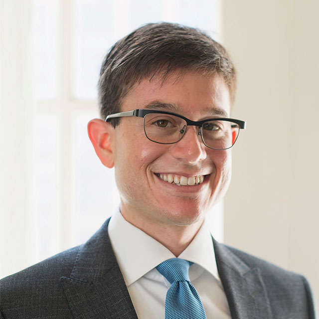 Steve Meth, in a formal portrait, wearing a gray suit jacket, white button down and light blue tie