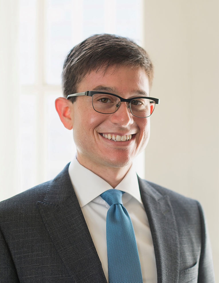 Steve Meth, in a formal portrait, wearing a gray suit jacket, white button down and light blue tie