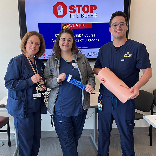 Judy Schroeder, Alyssa Kasraii and Zakk Arciaga stand in front of a TV that reads "Stop the Bleed" in red lettering.