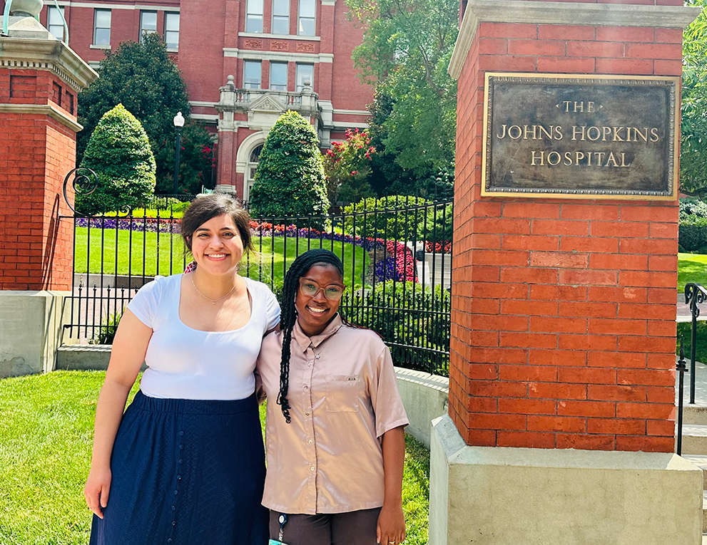 Melody Rorabeck and Kenara Ford standing in front of the gated entrance of The Johns Hopkins Hospital