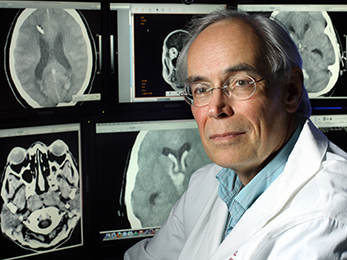 Portrait of Dan Hanley in front of screens displaying brain imaging