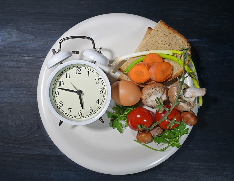 A clock, bread and vegetables pictured on a white plate